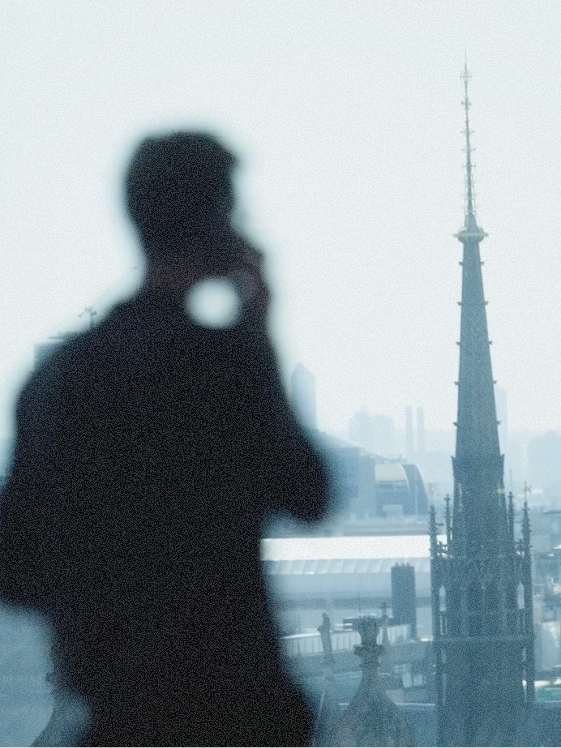A blurry silhouette of a person overlooking a misty cityscape featuring a prominent gothic spire.