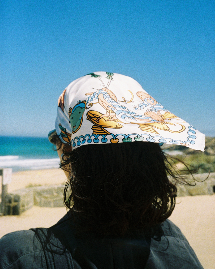 A woman facing the sea wearing a colourful bandana