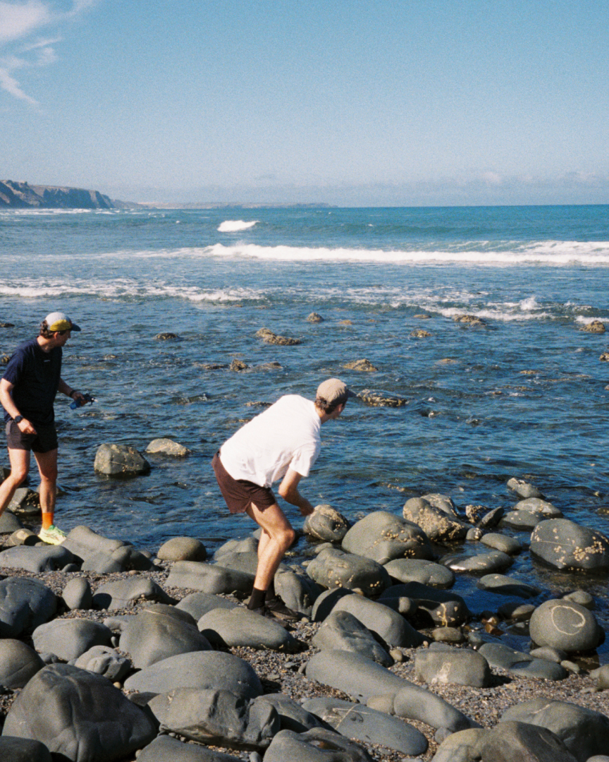 Two men play at throwing rocks to the ocean.